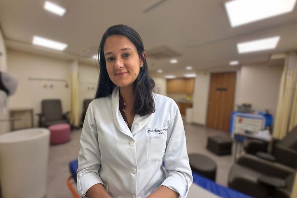 Médica de jaleco branco sorrindo em uma sala de atendimento